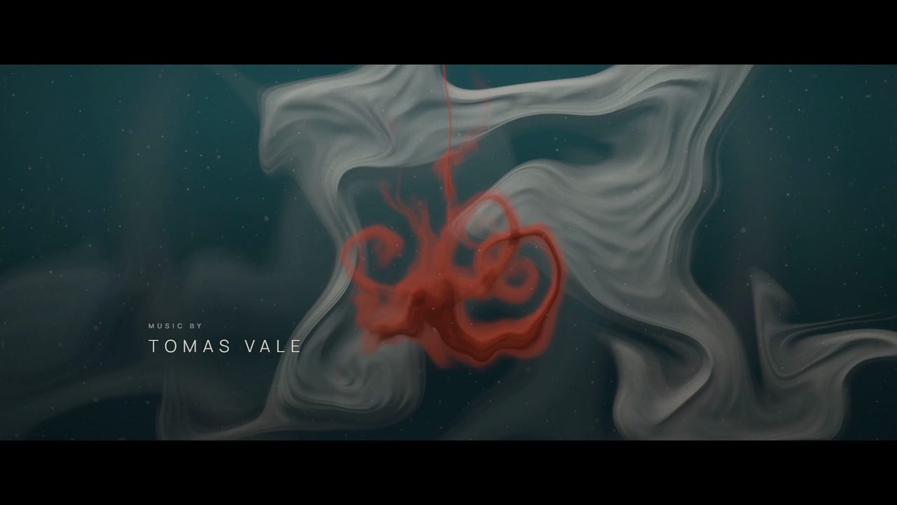 A rust-red drop of ink blooming through pale plumes in deep teal water